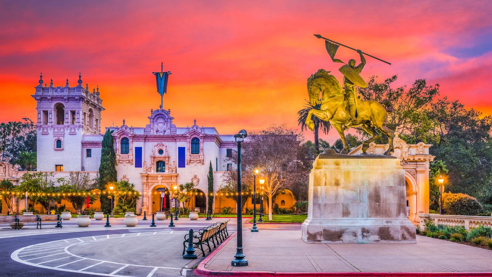 Horse and rider statue before a historic building at sunset, colorful sky and streetlights in Balboa Park, San Diego.