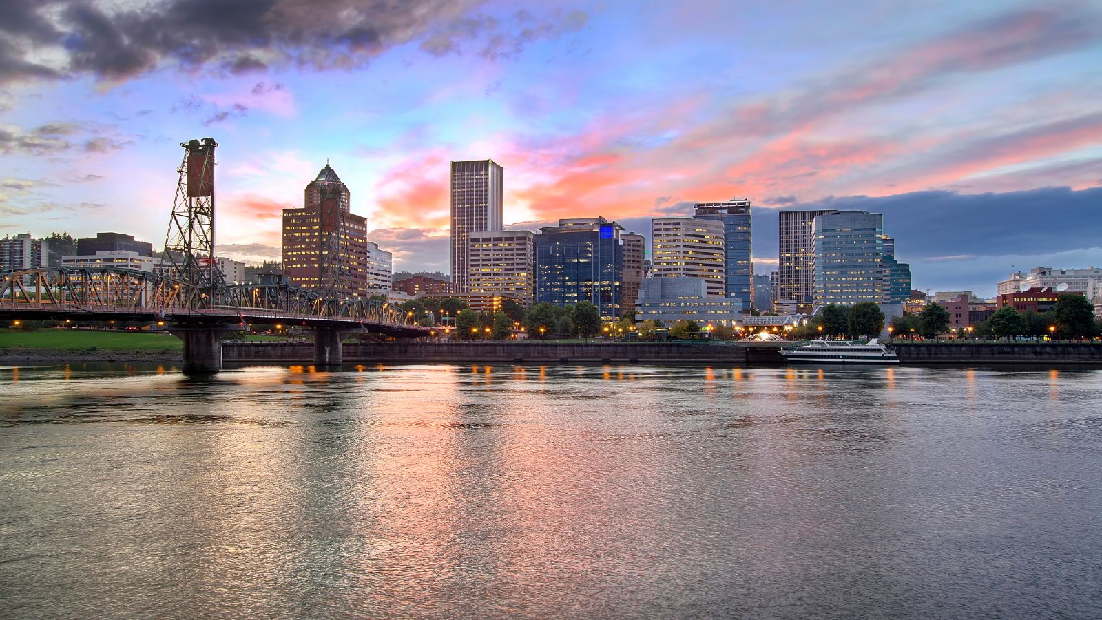 Portland skyline at sunset reflected in the river, featuring buildings, a bridge, and a vibrant sky.