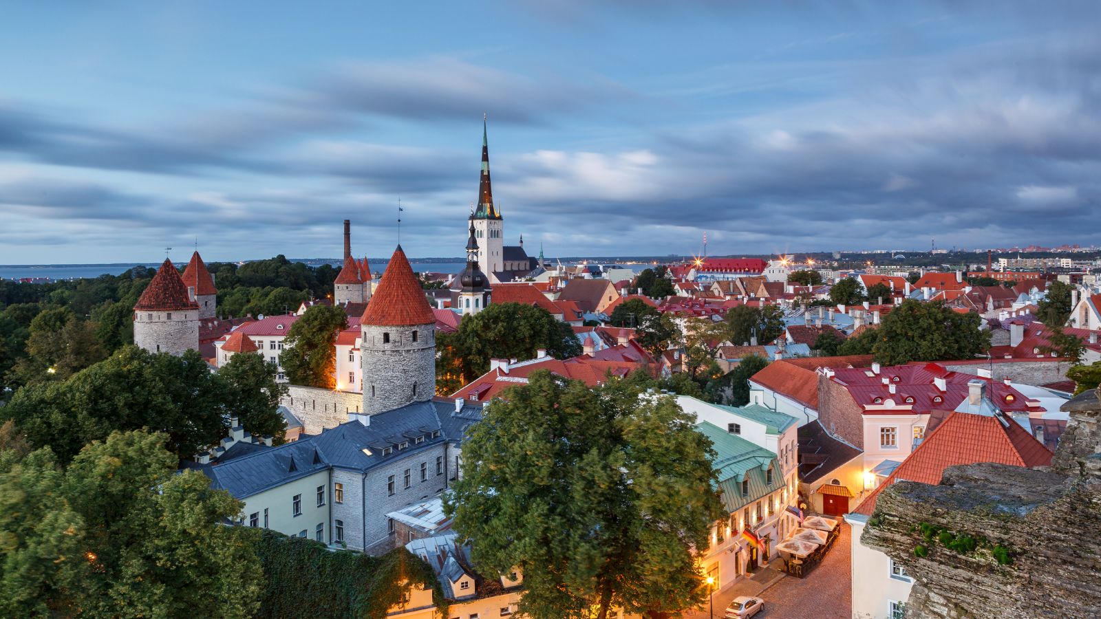 Tallinn’s Old Town with medieval towers, red roofs, and a tall church spire beneath a cloudy evening sky.
