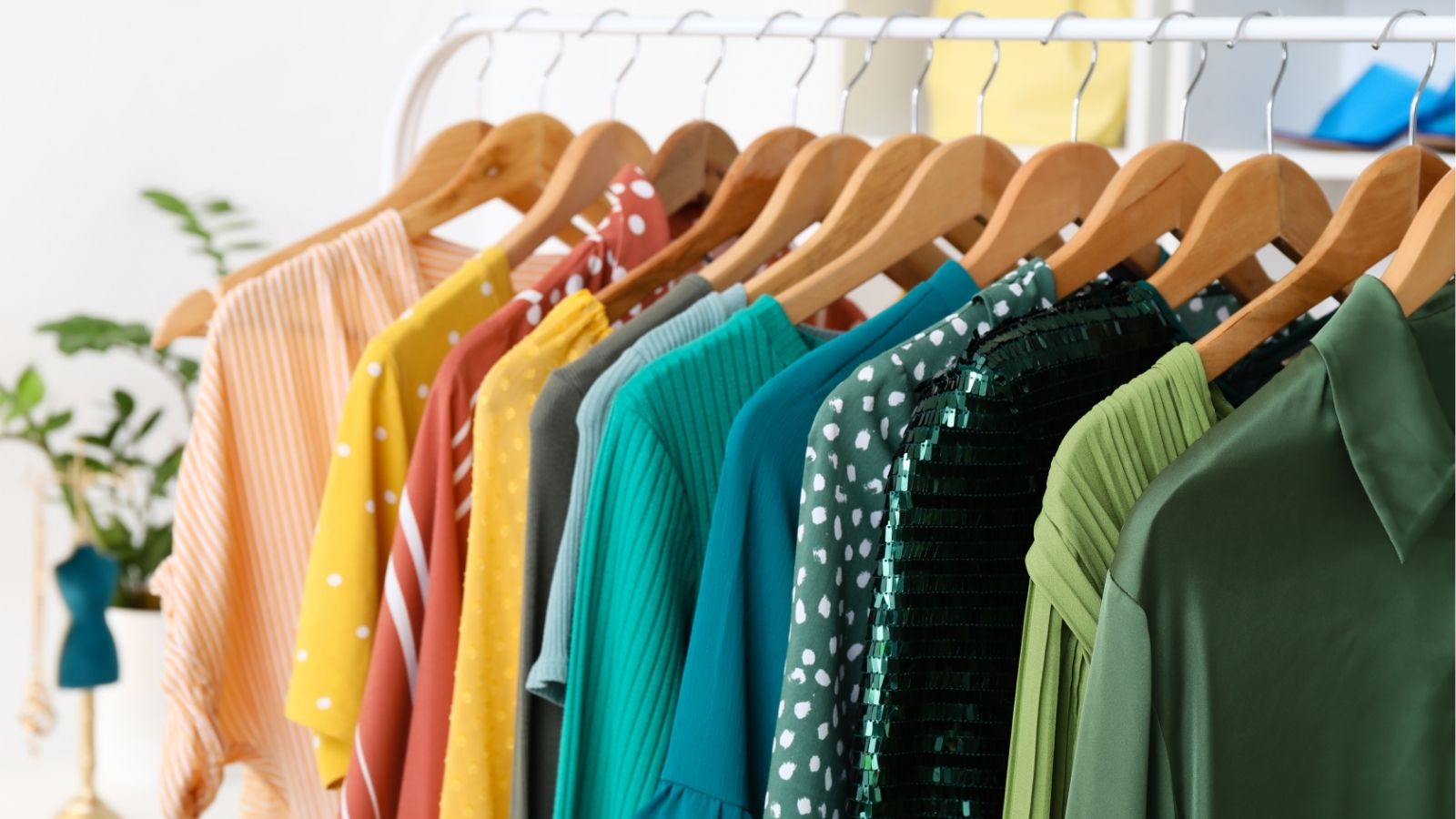 A clothing rack holds colorful shirts and dresses in yellow, pink, blue, green, and teal, some with polka dots or sequins.