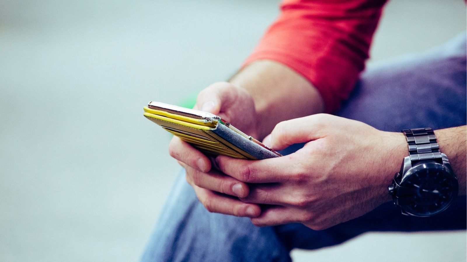 A person in a red sleeve and wristwatch uses a yellow-cased smartphone.