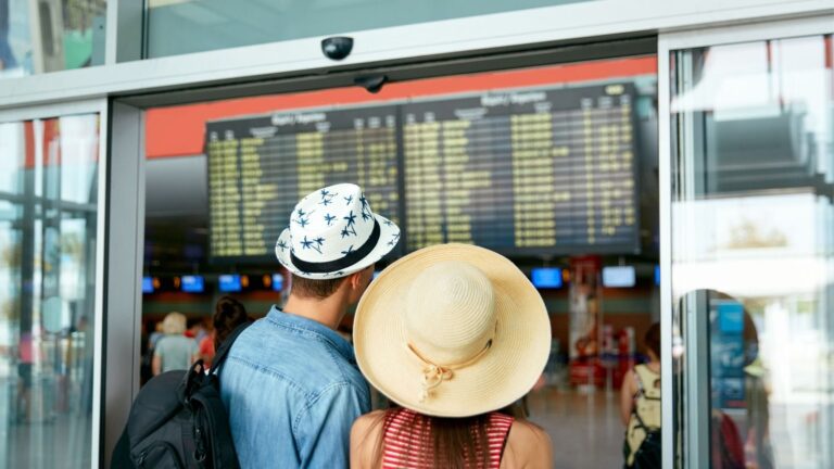 A man and a woman looking at the sign board while travelling.