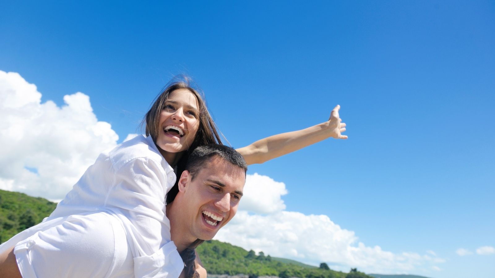 A woman riding on a man's back with a clear blue sky behind them.