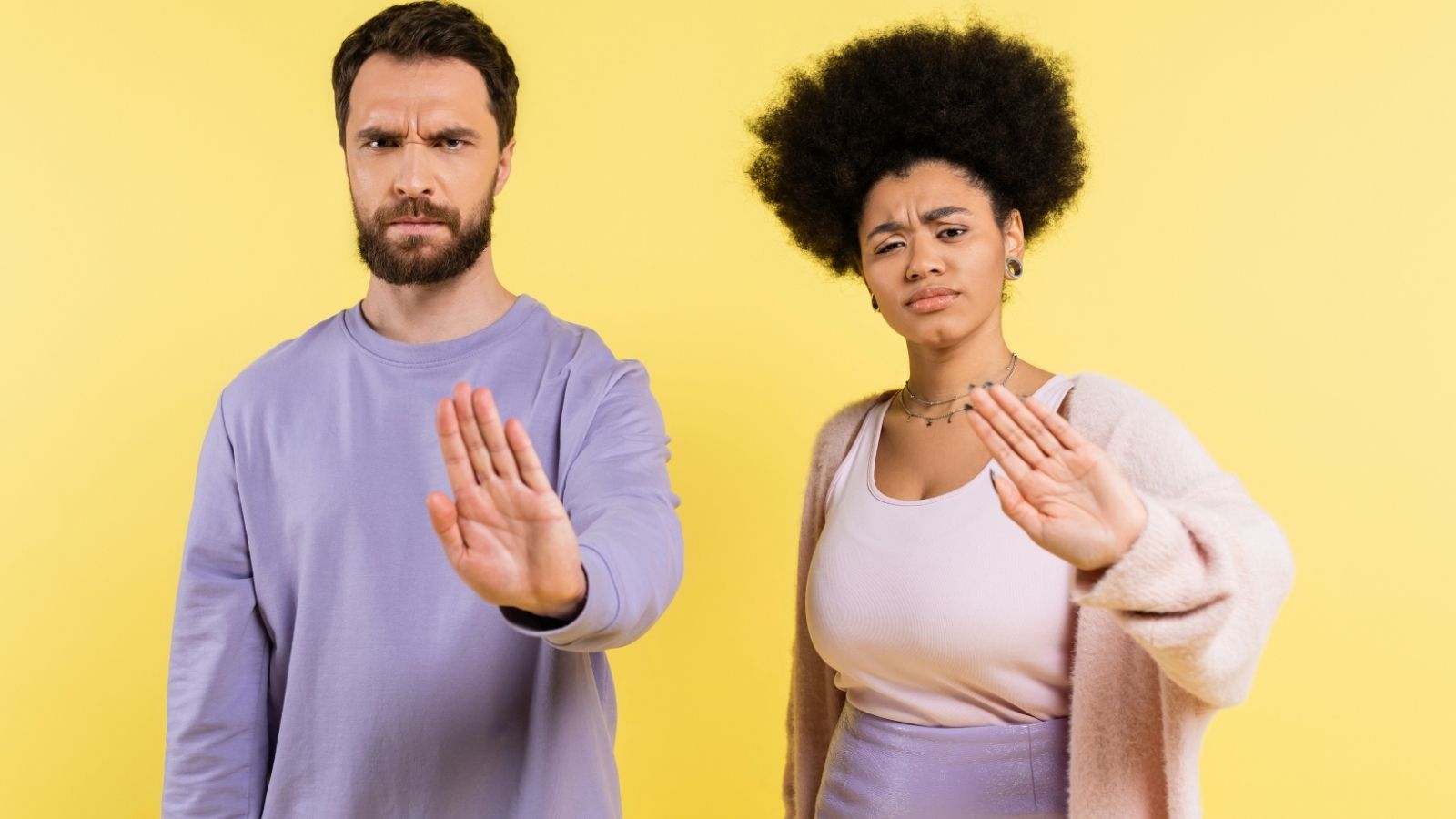 A picture of a man and a woman with one hand up, palms facing the camera gesturing stop.