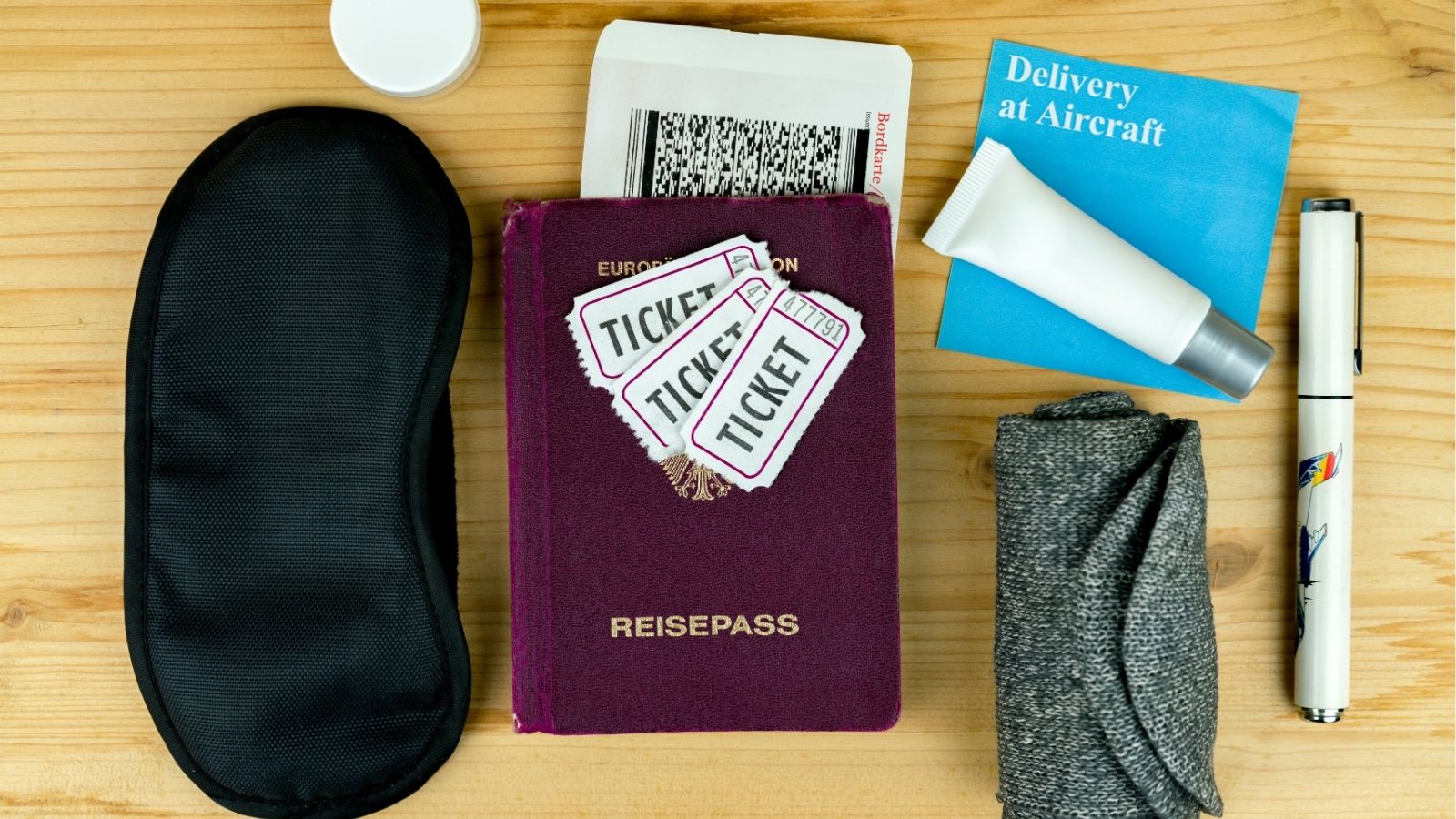 Travel essentials including a passport, tickets, and personal items are neatly laid out on a wooden surface.