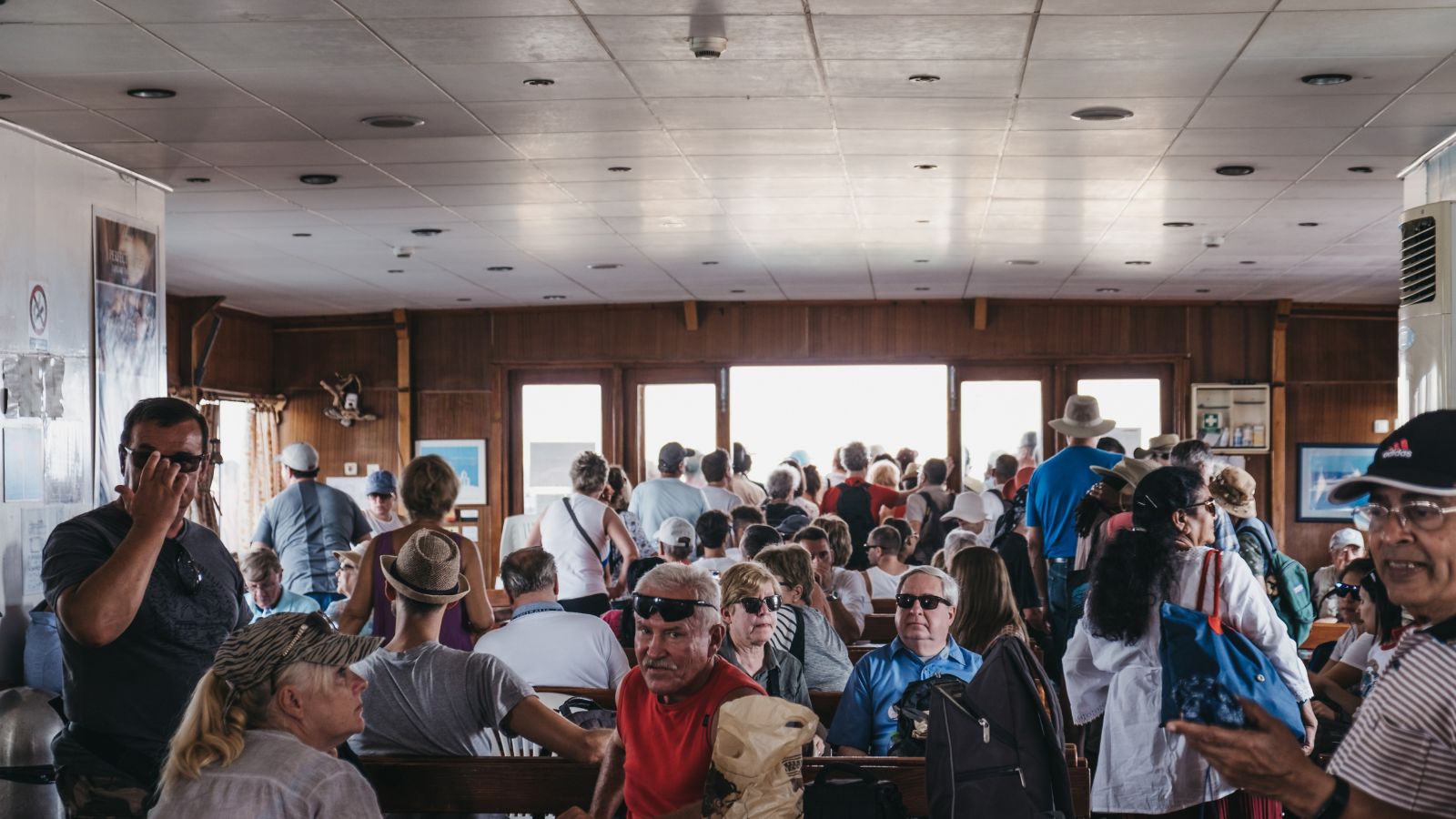 A photo of a cruise packed with passengers from different ages, some are sitting and some are standing.