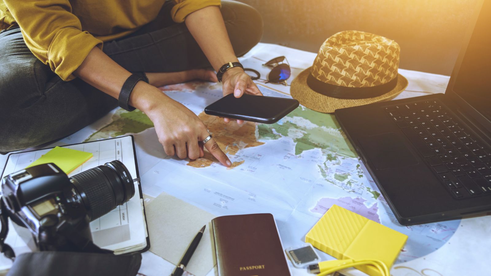 A photo of Overhead view of travel planning in progress: open passport, printed documents, maps, phone with transit app, laptop showing flight or visa information.
