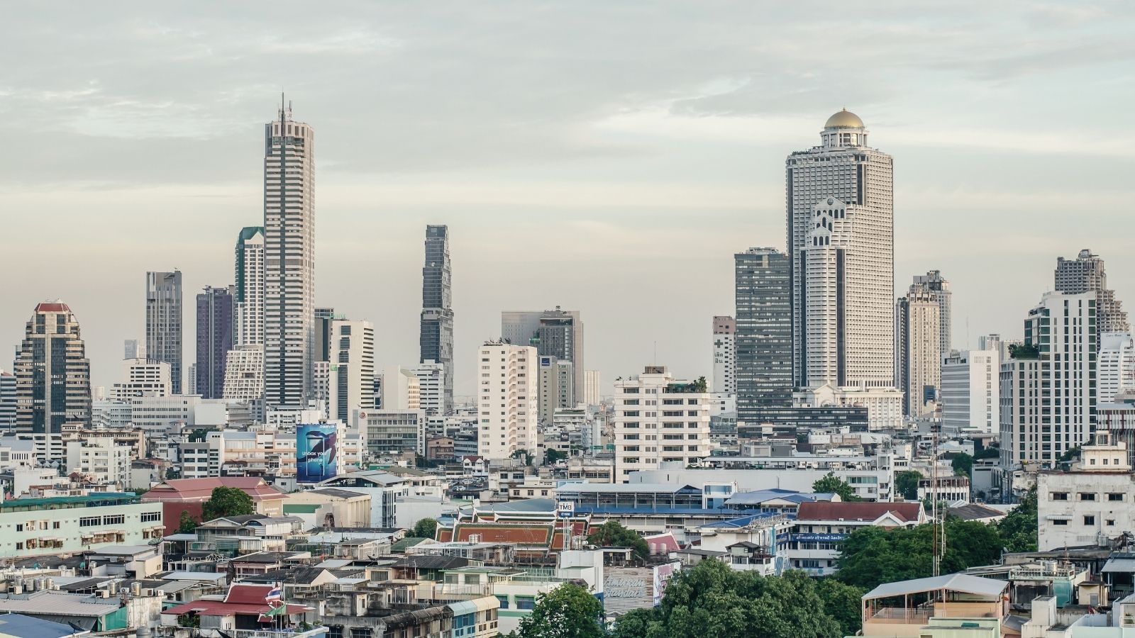 Modern high-rise buildings and skyscrapers form a cityscape beneath a mostly cloudy sky.