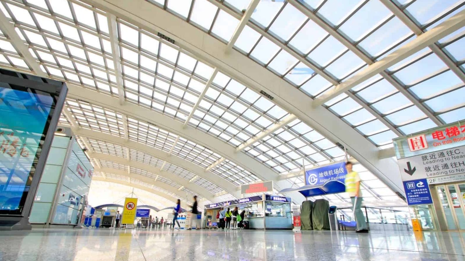 Modern train station with high glass ceiling, ticket gates, Chinese signs, and blurred people on a polished floor.