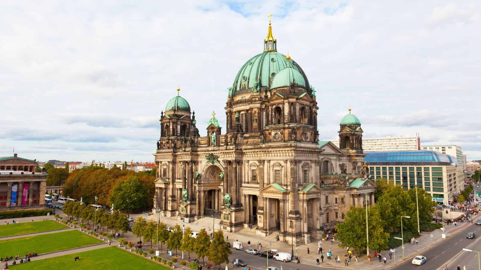 Historic cathedral with green dome and ornate details, bordered by streets and greenery beneath a partly cloudy sky.