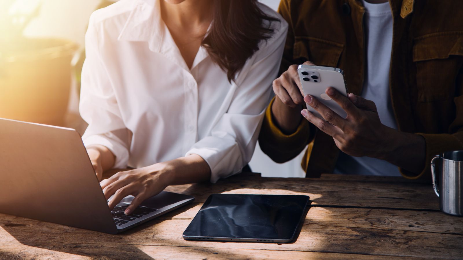 A photo of One partner focused on planning travel on a laptop while the other scrolls on phone nearby.