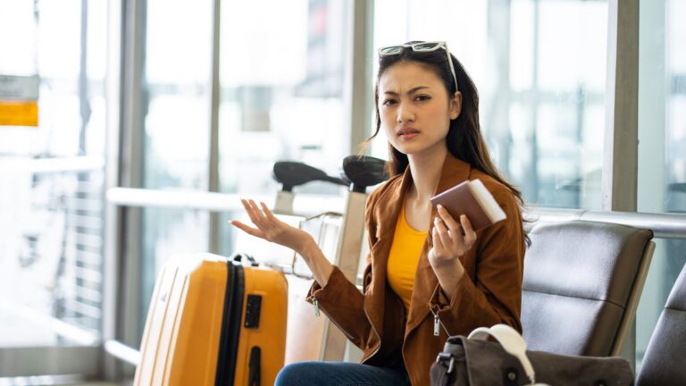 A woman sits on a bench beside her luggage.