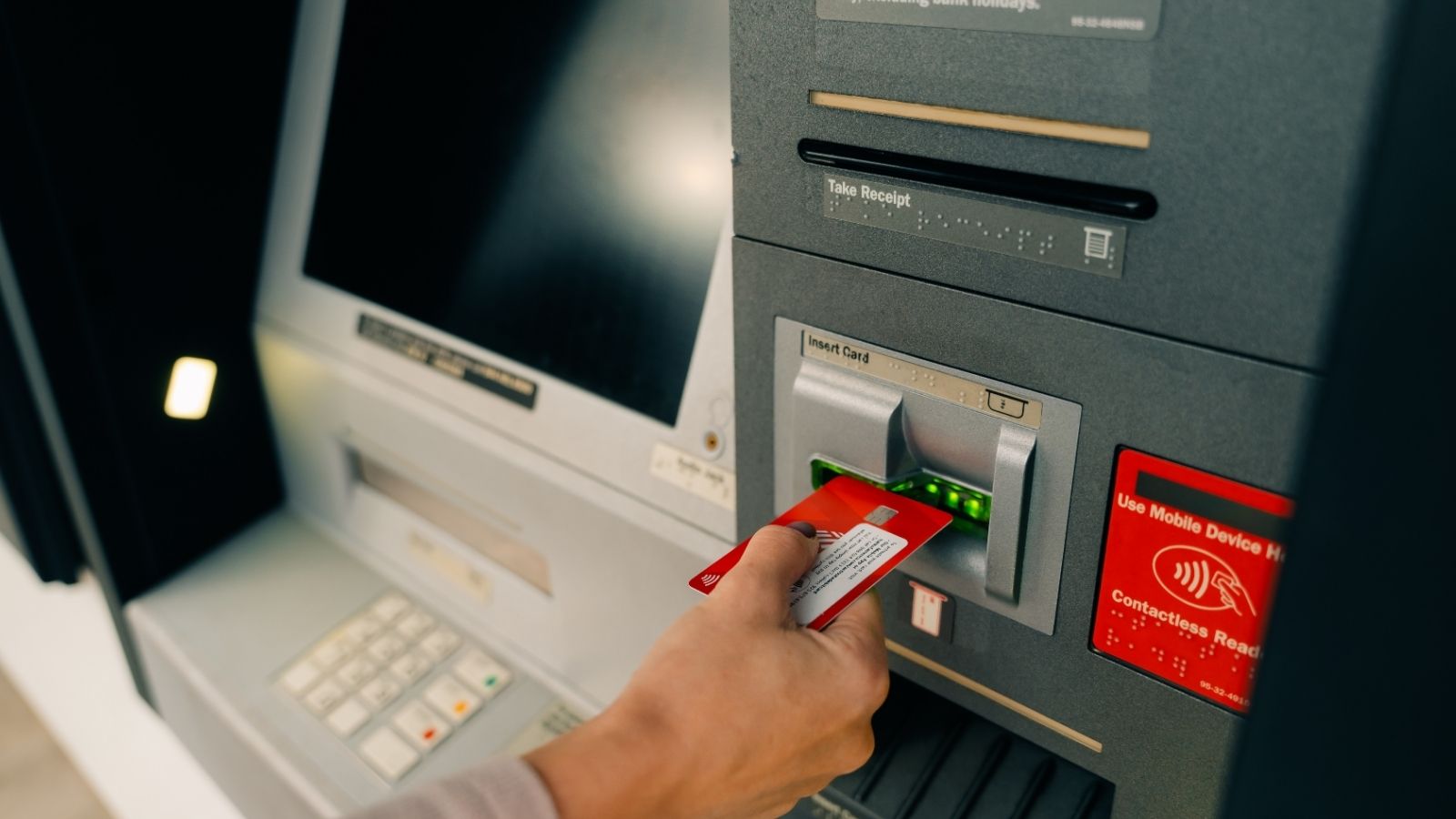 A person inserts a bank card into an ATM slot.