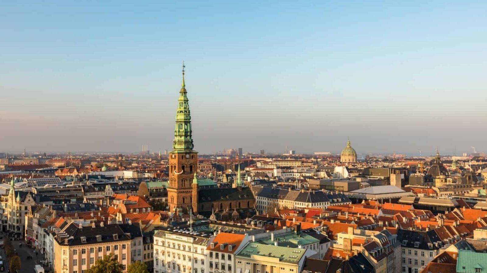 Panoramic view of a European city with historic buildings, colorful rooftops, and a tall church tower under a clear sky.