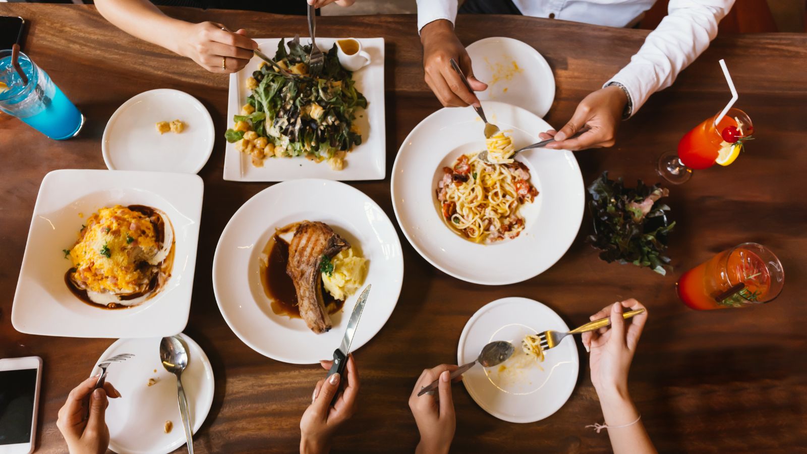 A photo of Overhead view of a table with multiple dishes from a foreign cuisine, some partially eaten, drinks and utensils around.
