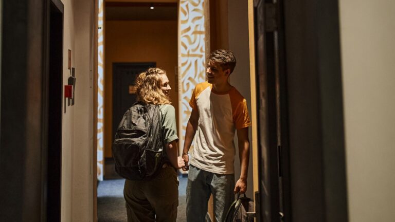 A couple talking to each other as they enter a hotel room.