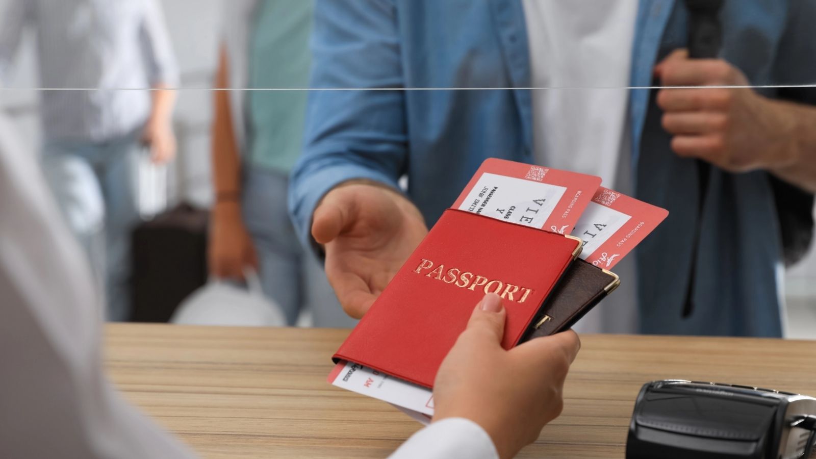 At a check-in counter, a person gives a red passport and boarding passes to an airline staff member.