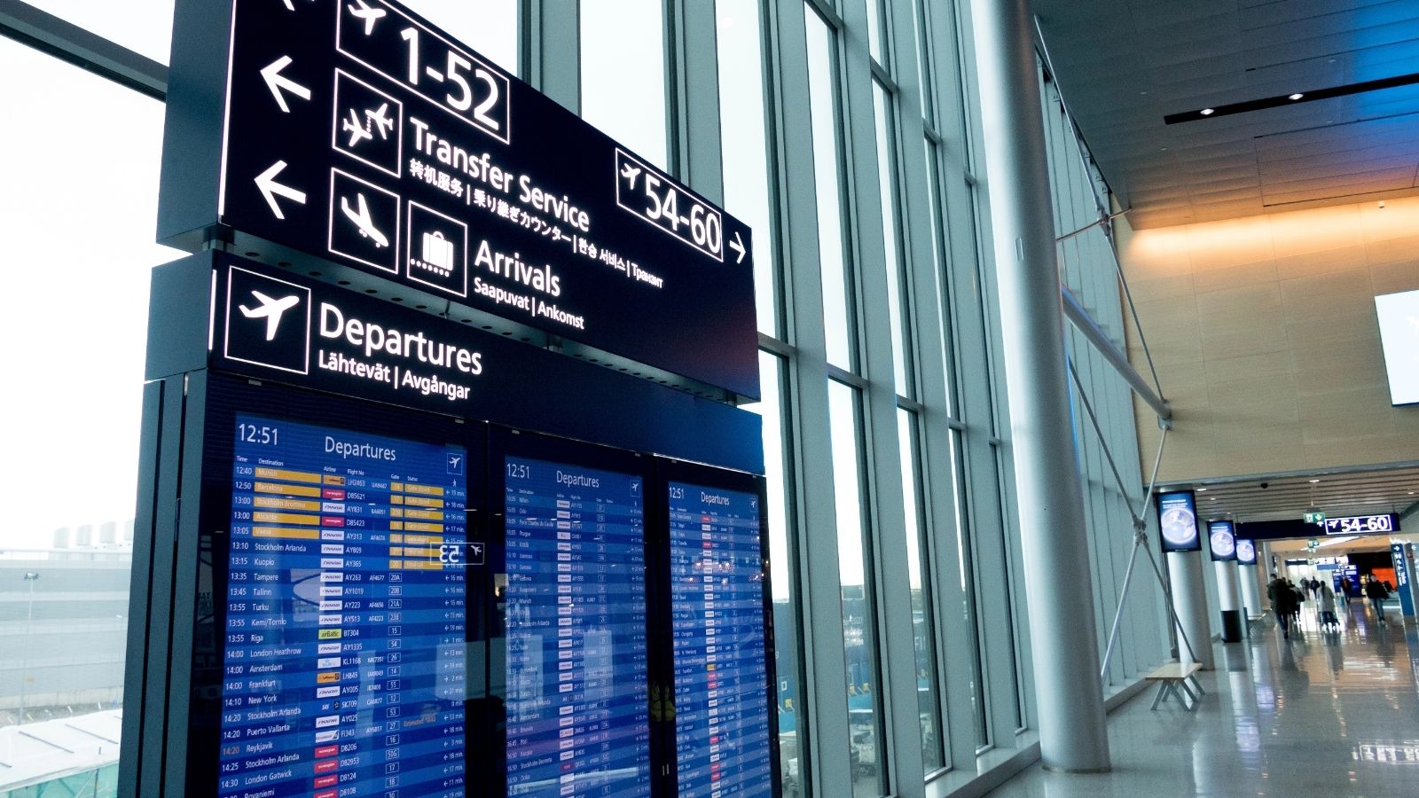 Airport terminal with digital departure boards, signs for arrivals and departures, and large windows letting in natural light.