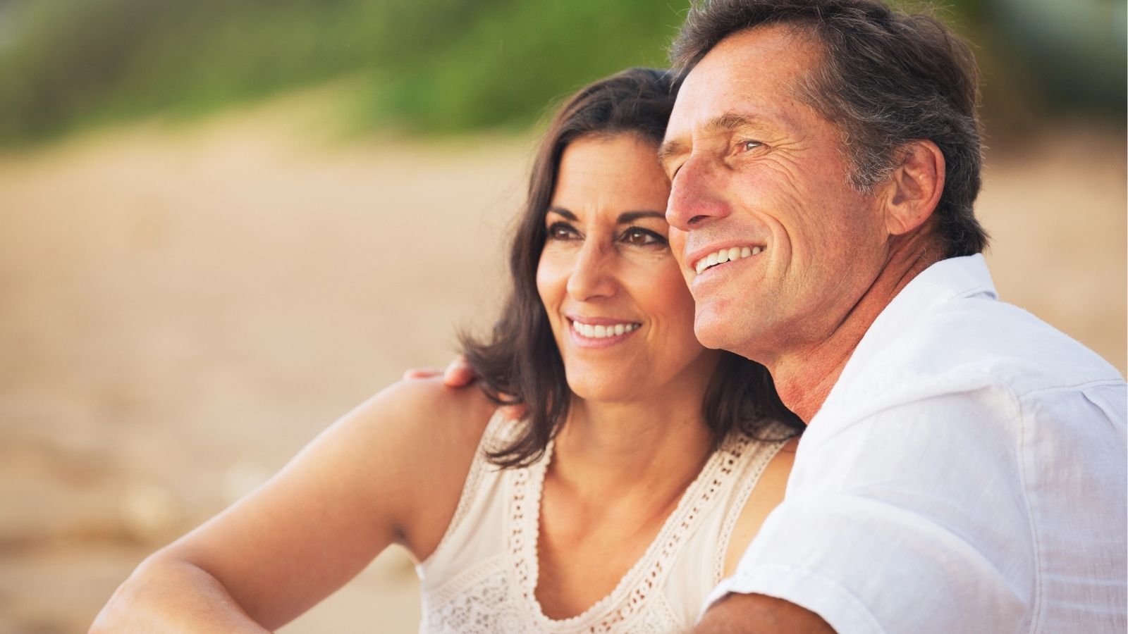 A man and woman sitting and smiling by the beach.