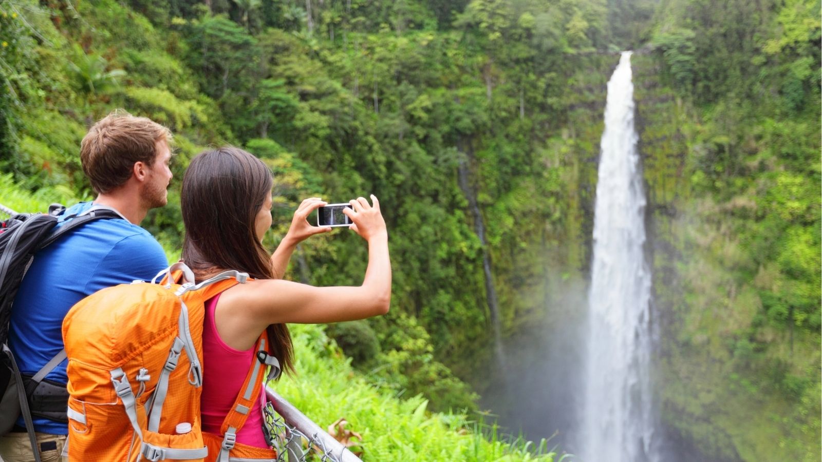 A man and a woman taking a picture of a waterfall in Hawaii.