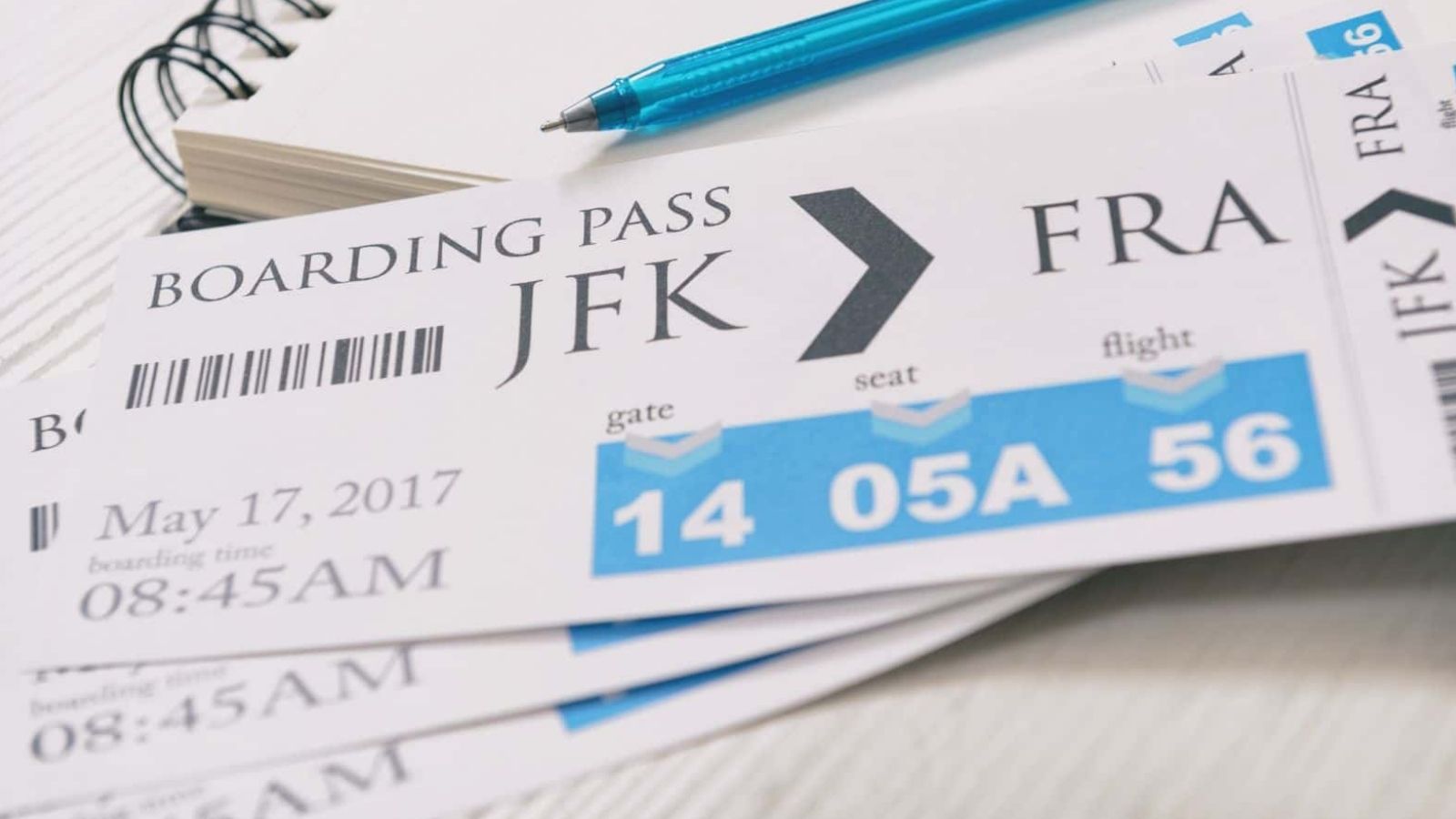 Boarding pass from JFK to FRA with gate 14, seat 05A, flight 56; pen and notebook visible in background.