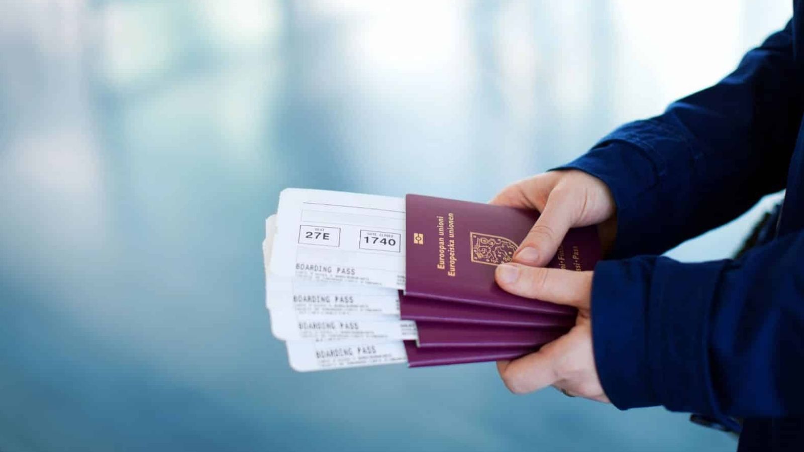 Person holds three EU passports and three boarding passes against a blurred background.