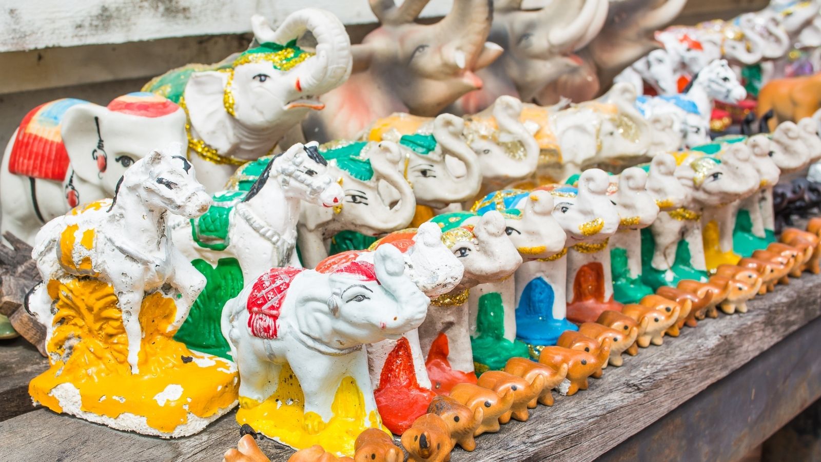 Colorful ceramic animal figurines, such as elephants and horses, are arranged in rows on a wooden surface.