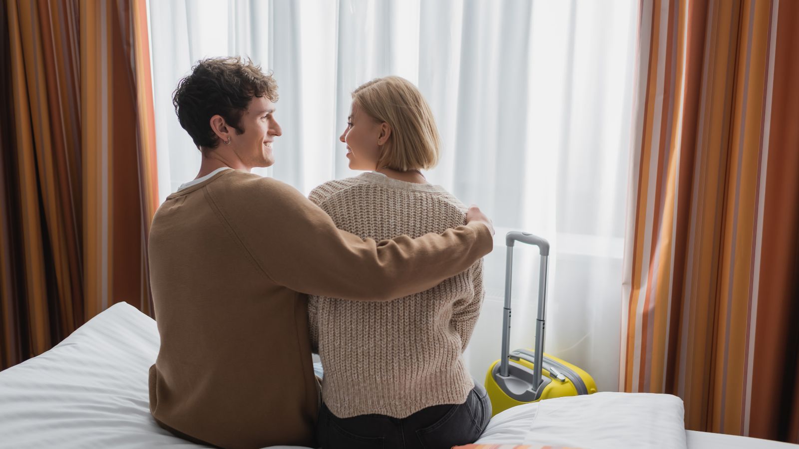 A picture of couple sitting in a bed looking at each other intently.