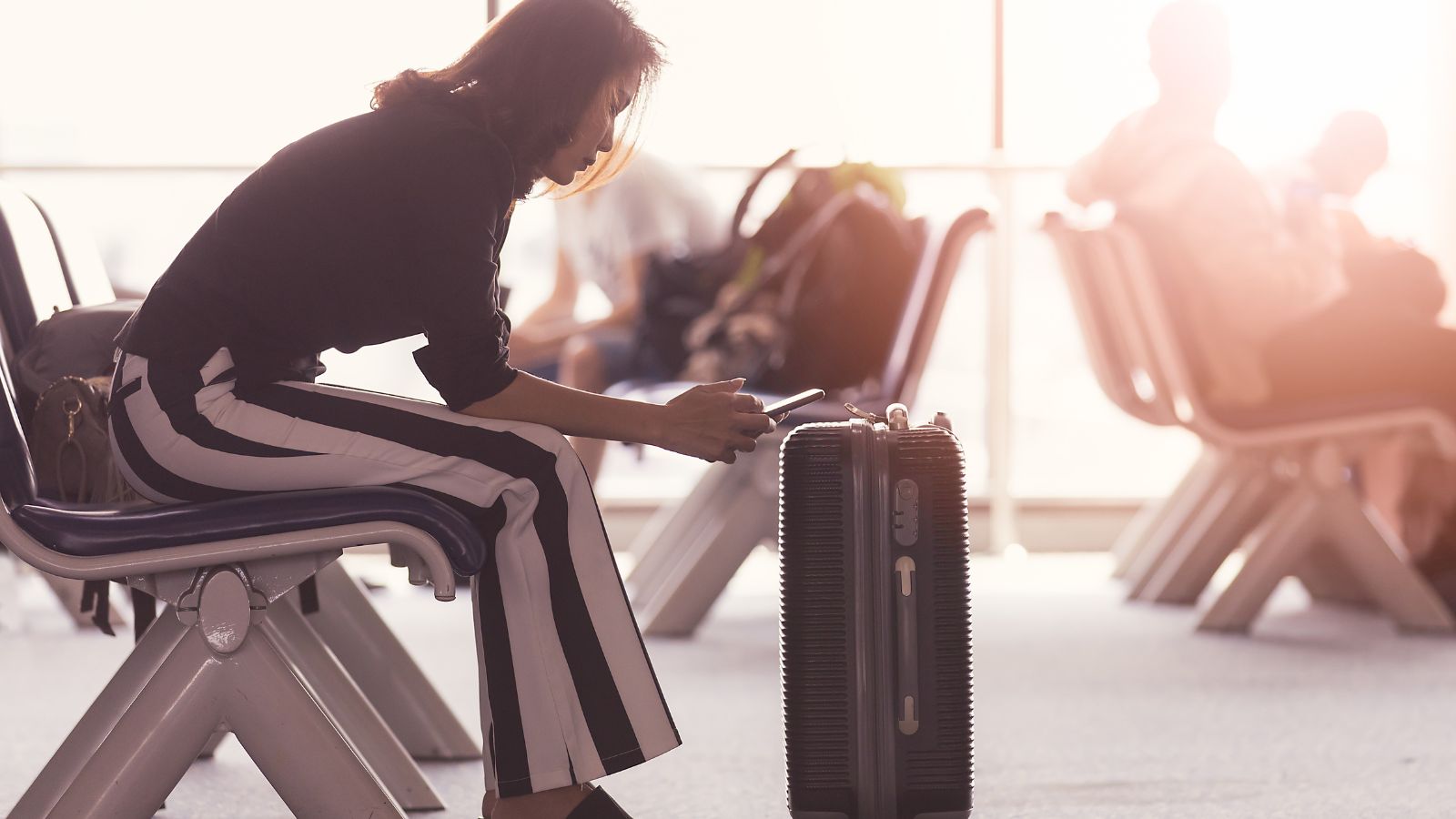 A photo of a woman busy with her cellphone and a luggage in front of her.
