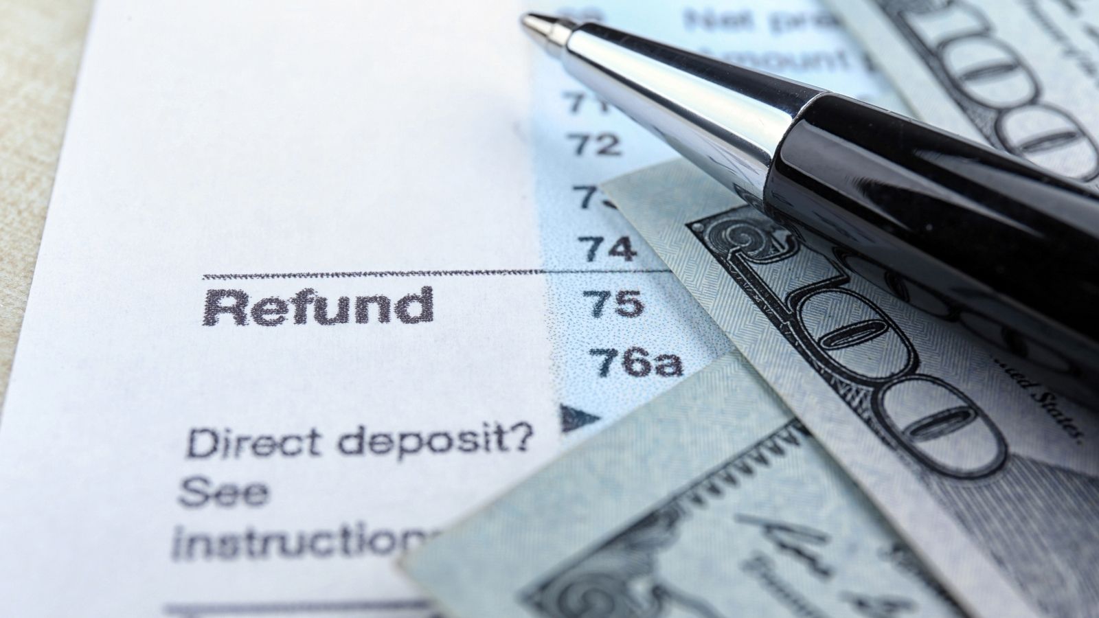Close-up of a tax document labeled "Refund," with a black pen and partially visible $100 bills.