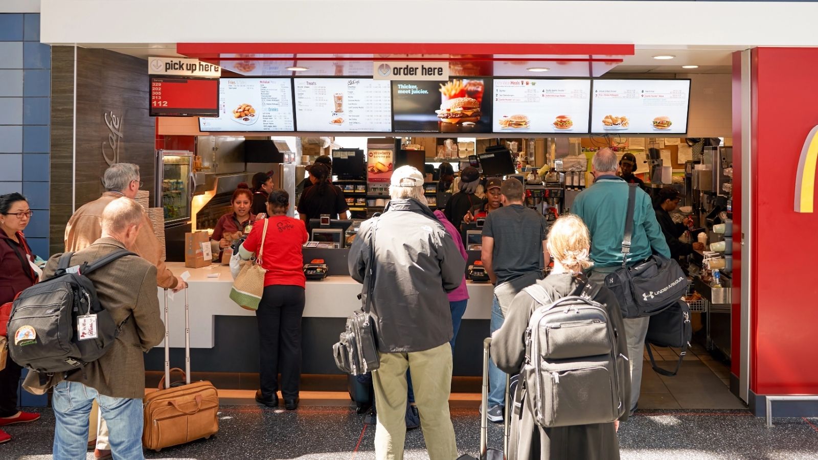People wait in line at a McDonald's counter with some ordering food and menu boards displayed above the registers.