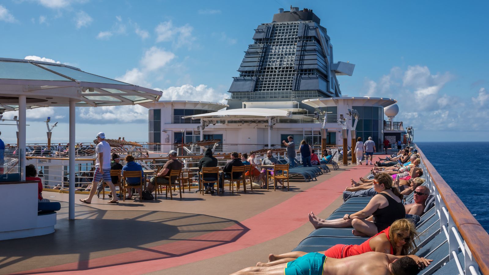 A photo of Cruise ship pool deck daytime, people reading and sunbathing, uncrowded, Caribbean sea in background.
