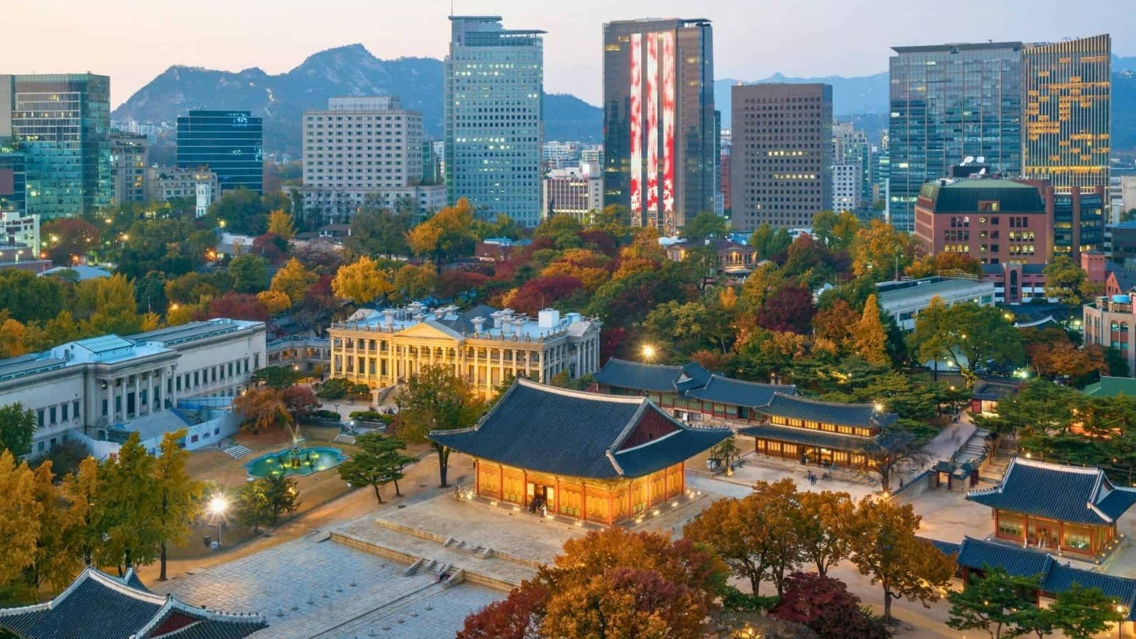 Aerial view of Deoksugung Palace amid autumn trees and skyscrapers in central Seoul, South Korea.