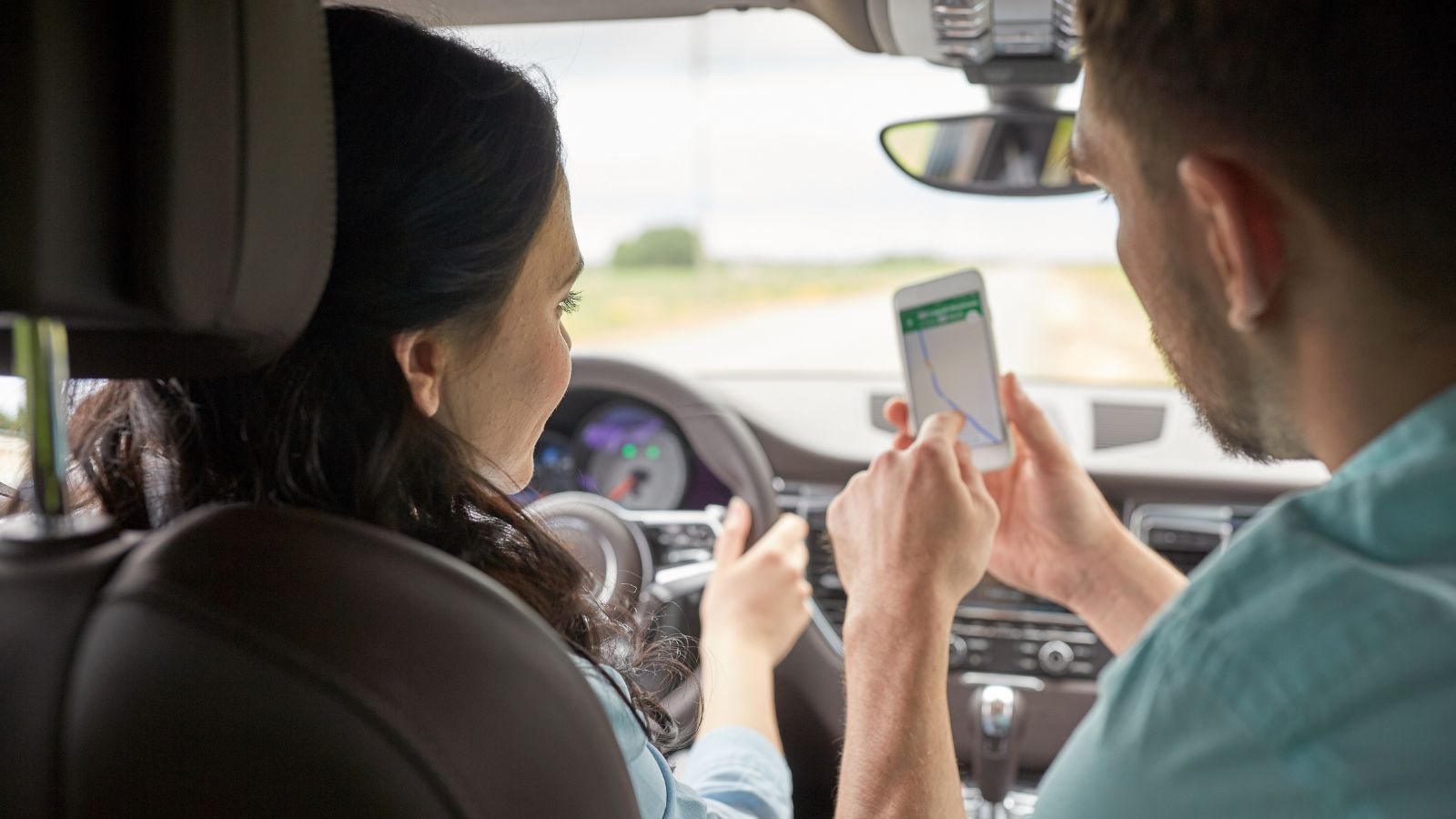 A couple in a car on a highway, one looking frustrated while the other glances at a GPS, natural light, realistic emotion, not exaggerated.