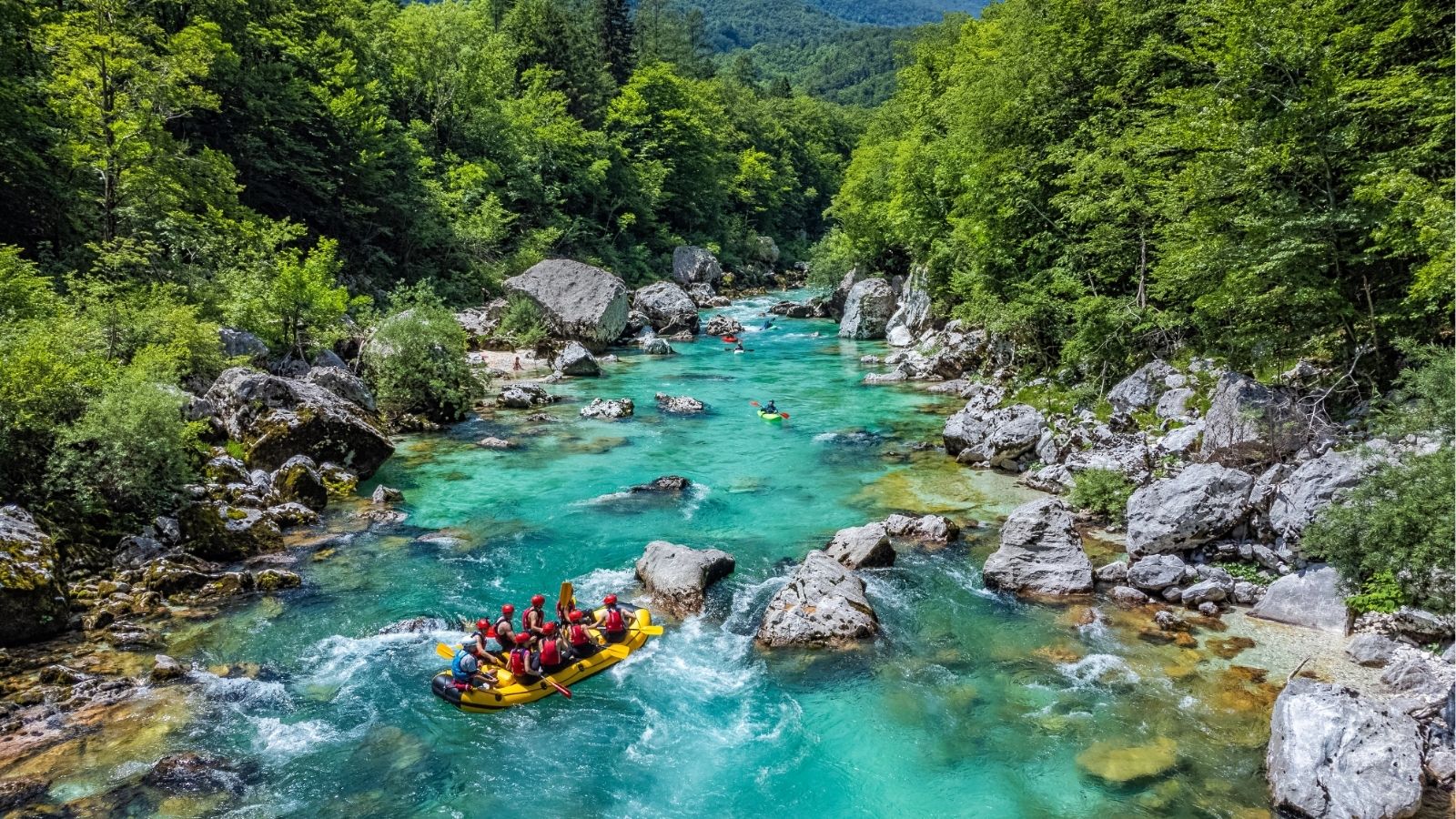 A yellow raft with people on a turquoise river passes through rocky terrain and dense green forest.