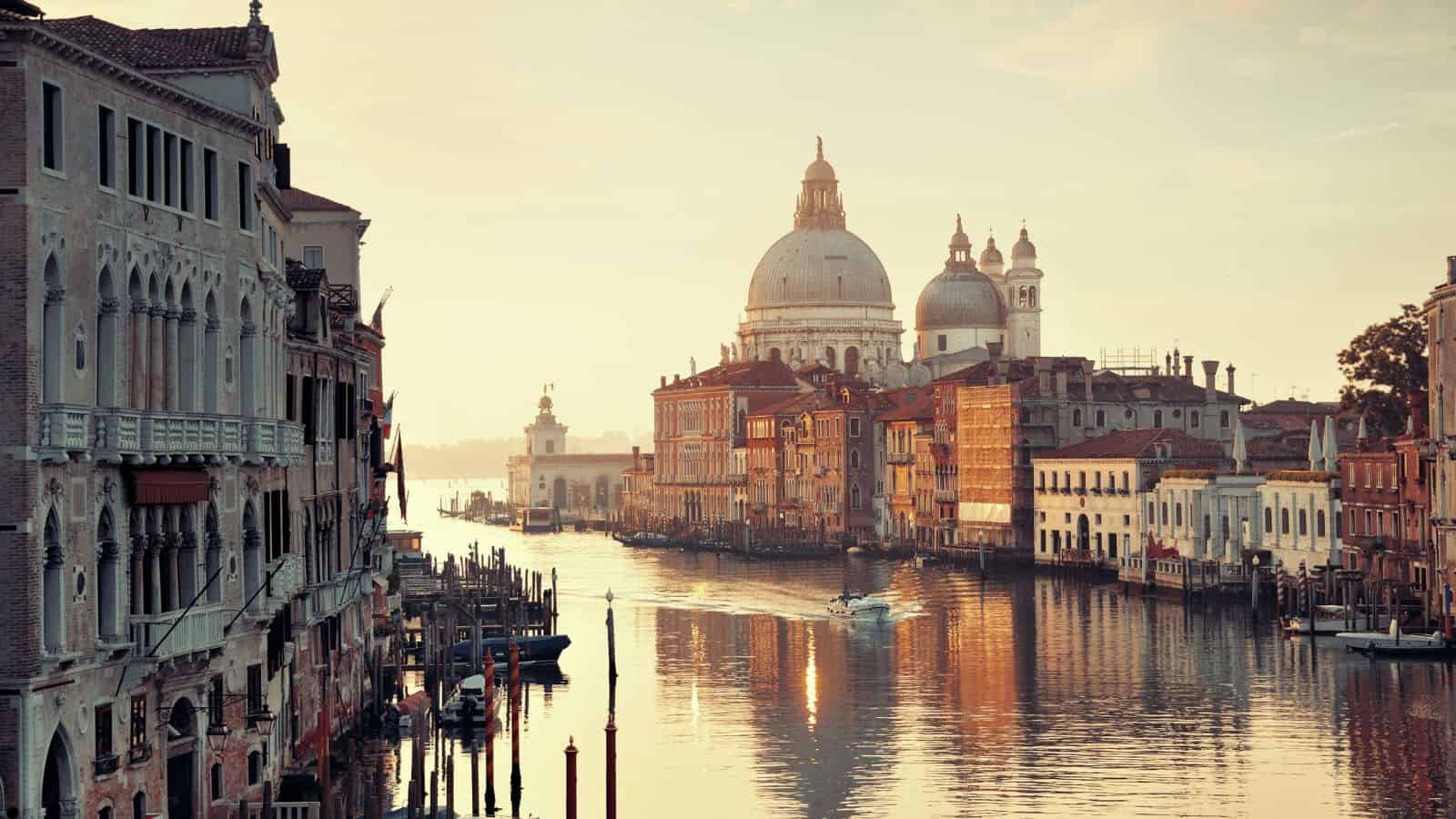 The Grand Canal in Venice at sunset, lined with historic buildings and Santa Maria della Salute's domes in the background.
