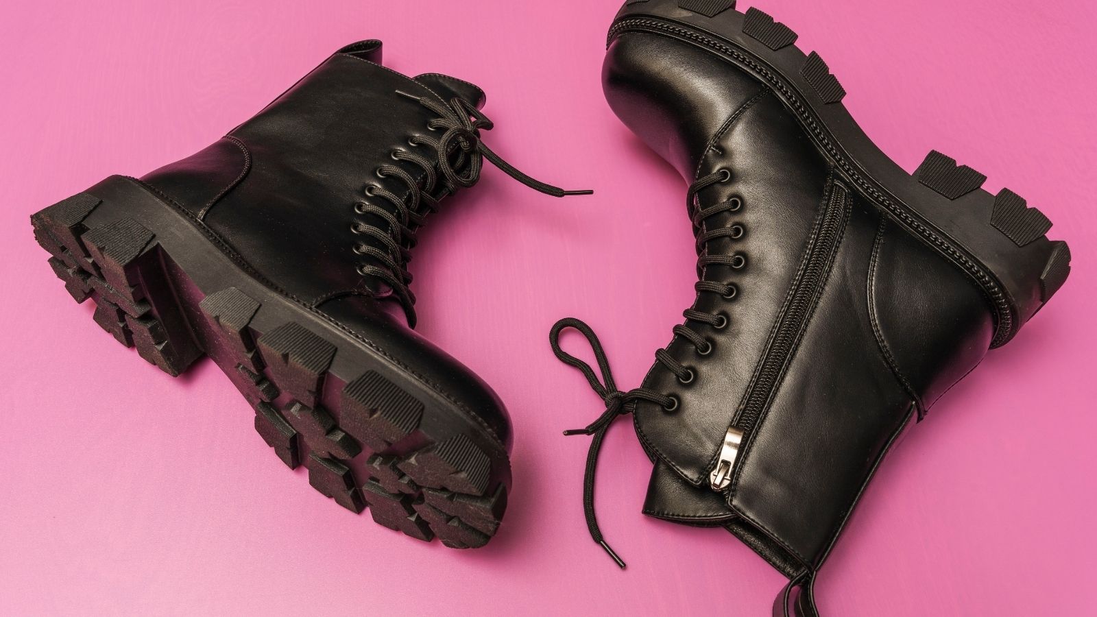 Black lace-up combat boots with thick soles and side zippers on a pink background.