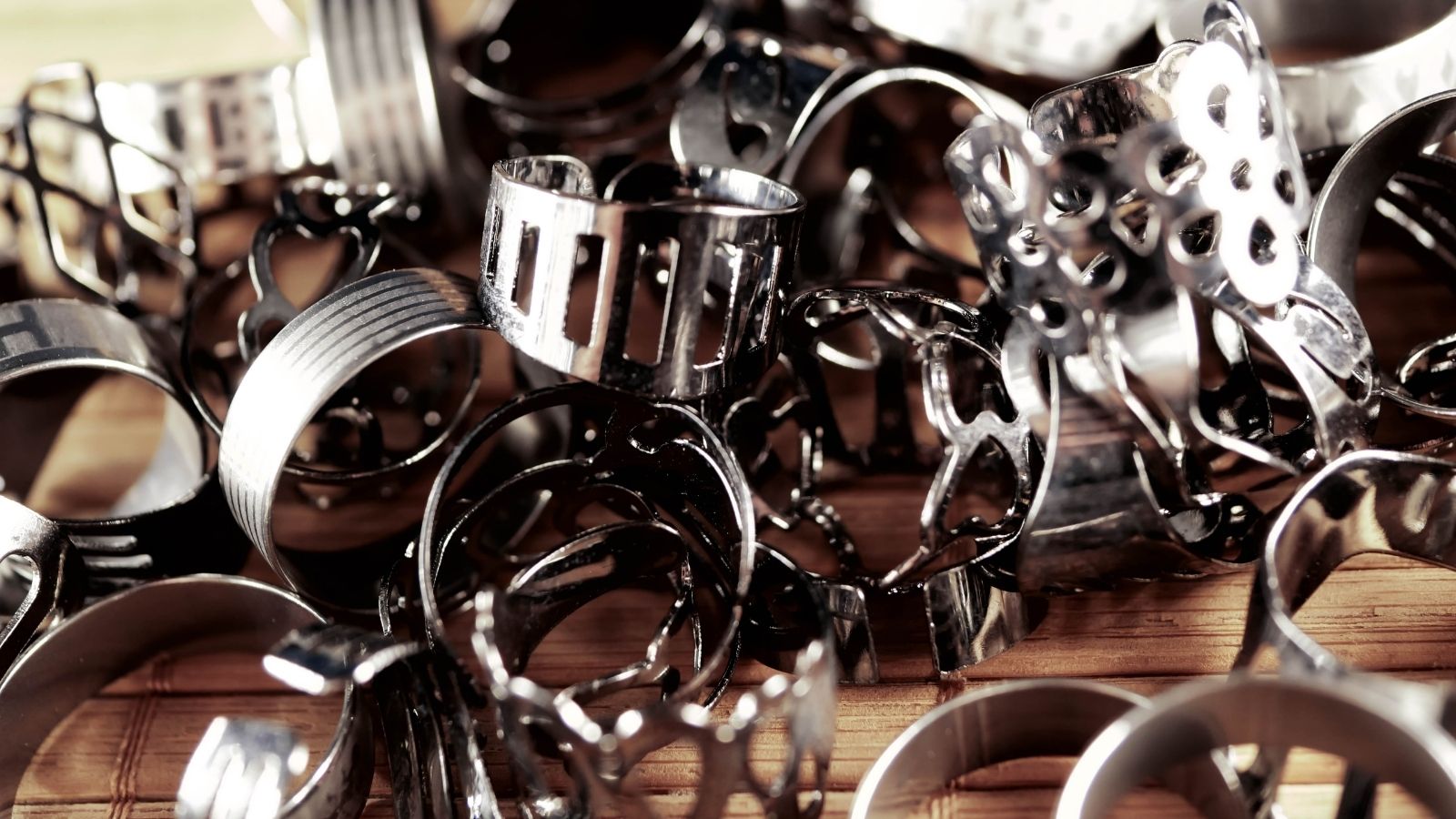 Assorted shiny metal rings and pastry molds piled close together on a wooden surface.