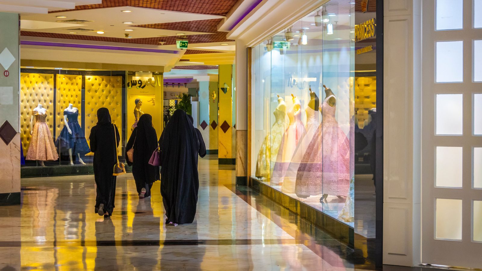 A photo of Tourists walking in Abu Dhabi shopping mall; people dressed modestly with covered shoulders and knees; cultural awareness.