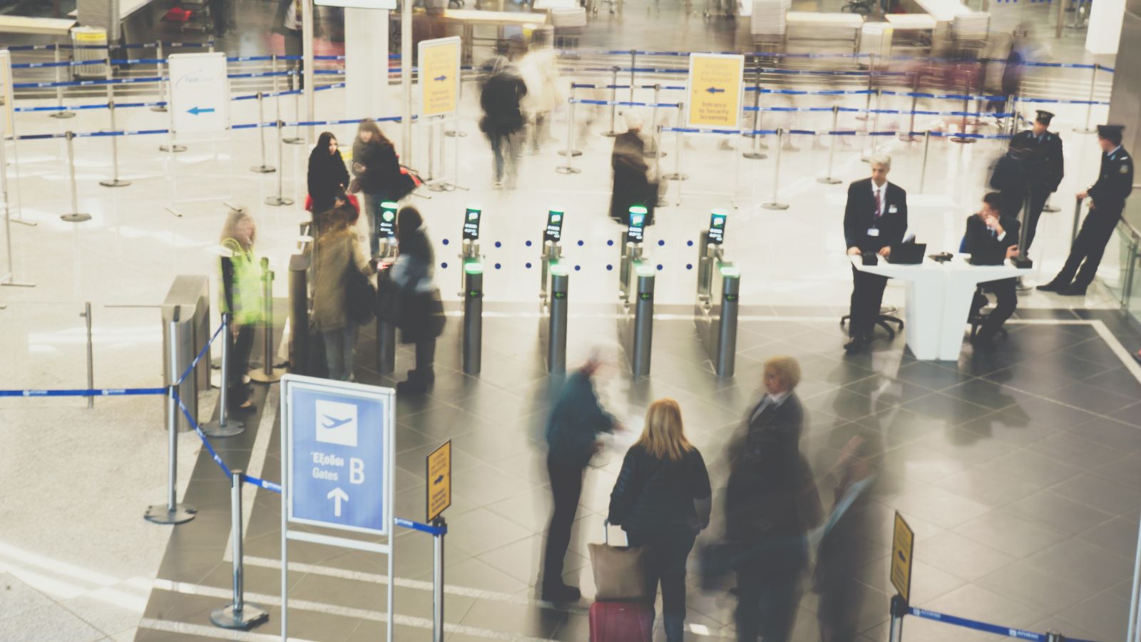 Travelers line up at an airport security checkpoint as staff oversee and direct them through gates.