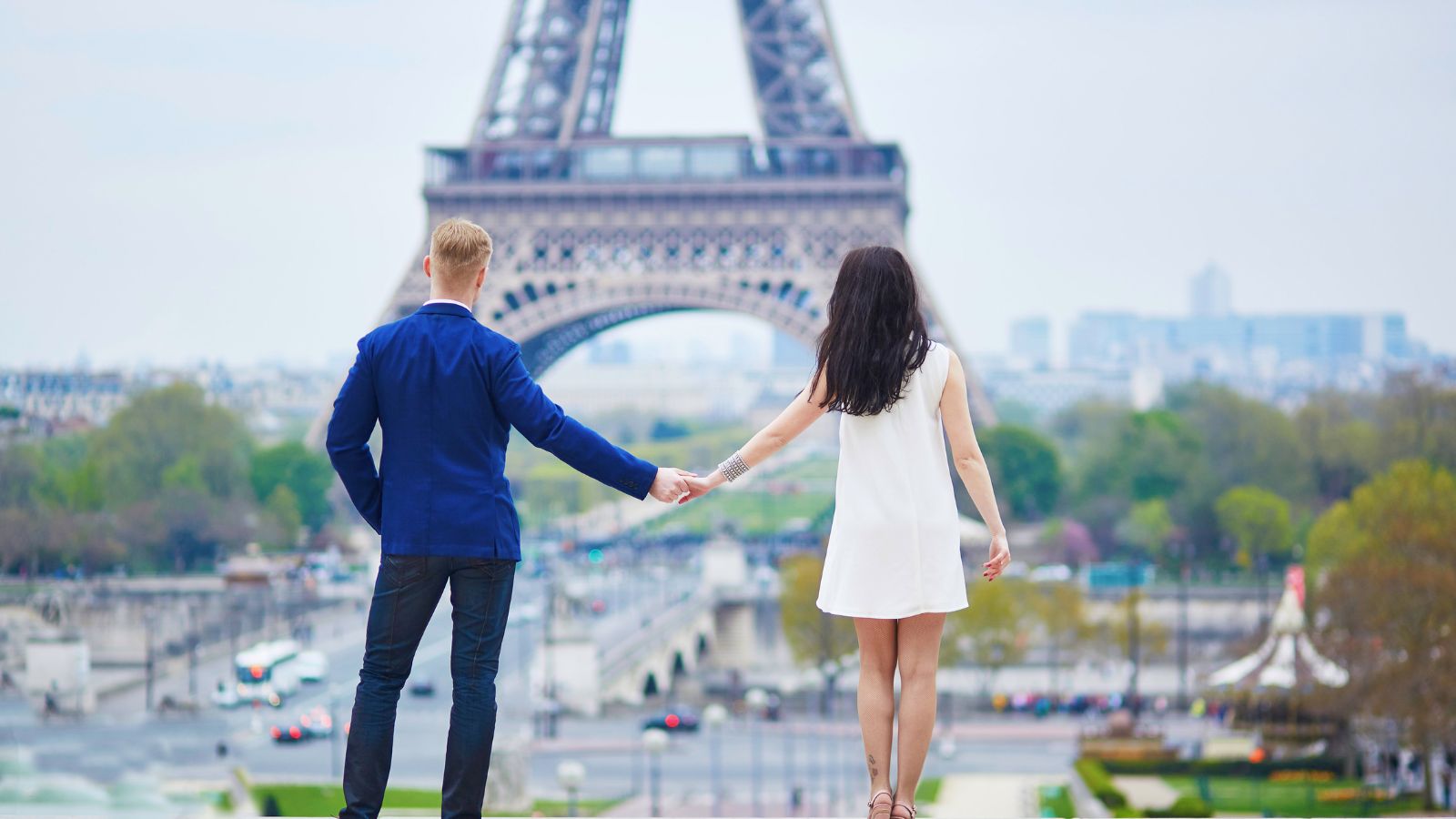A back photo of couple holding hands facing eiffel tower.