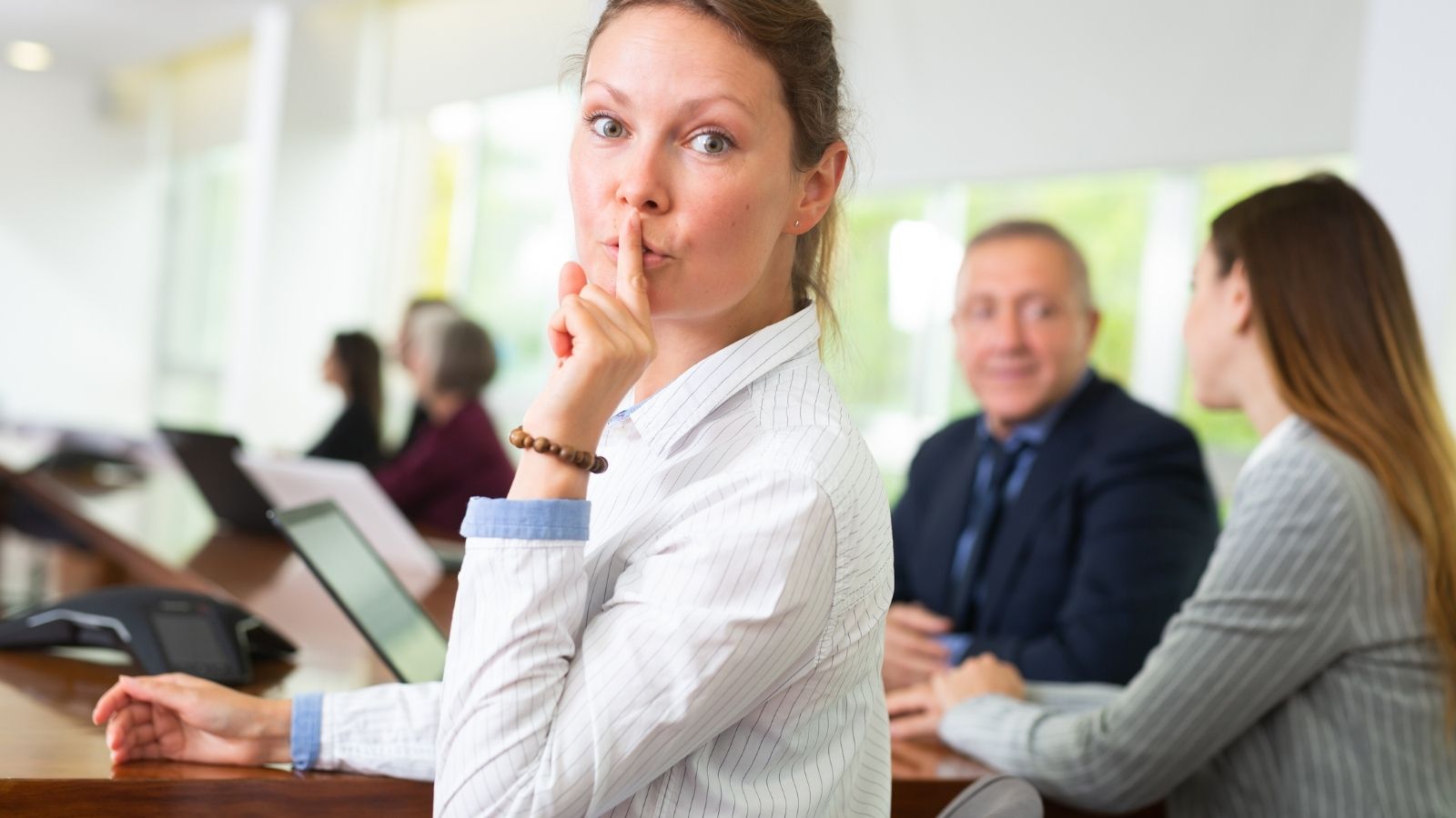 A woman makes a ‘shh’ gesture toward the camera.