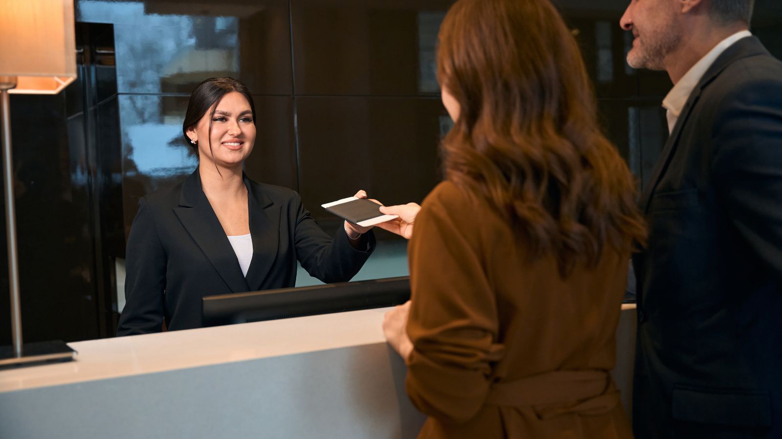 A photo of a couple handling a document to a front desk.
