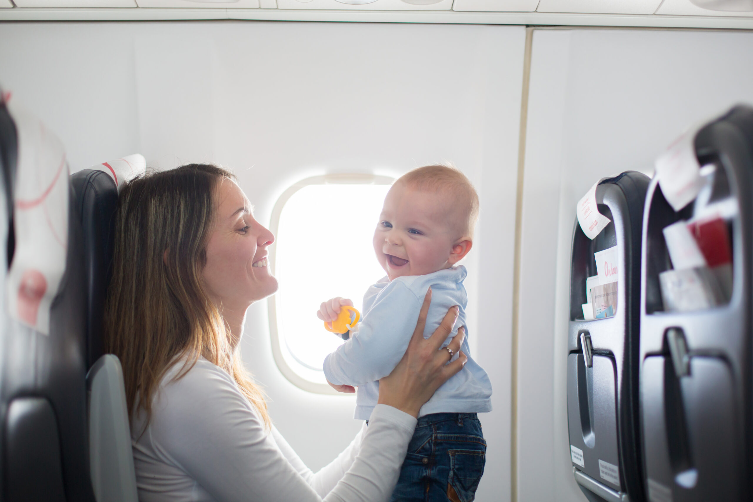 Young mom, playing and breastfeeding her toddler boy on board of aircraft.