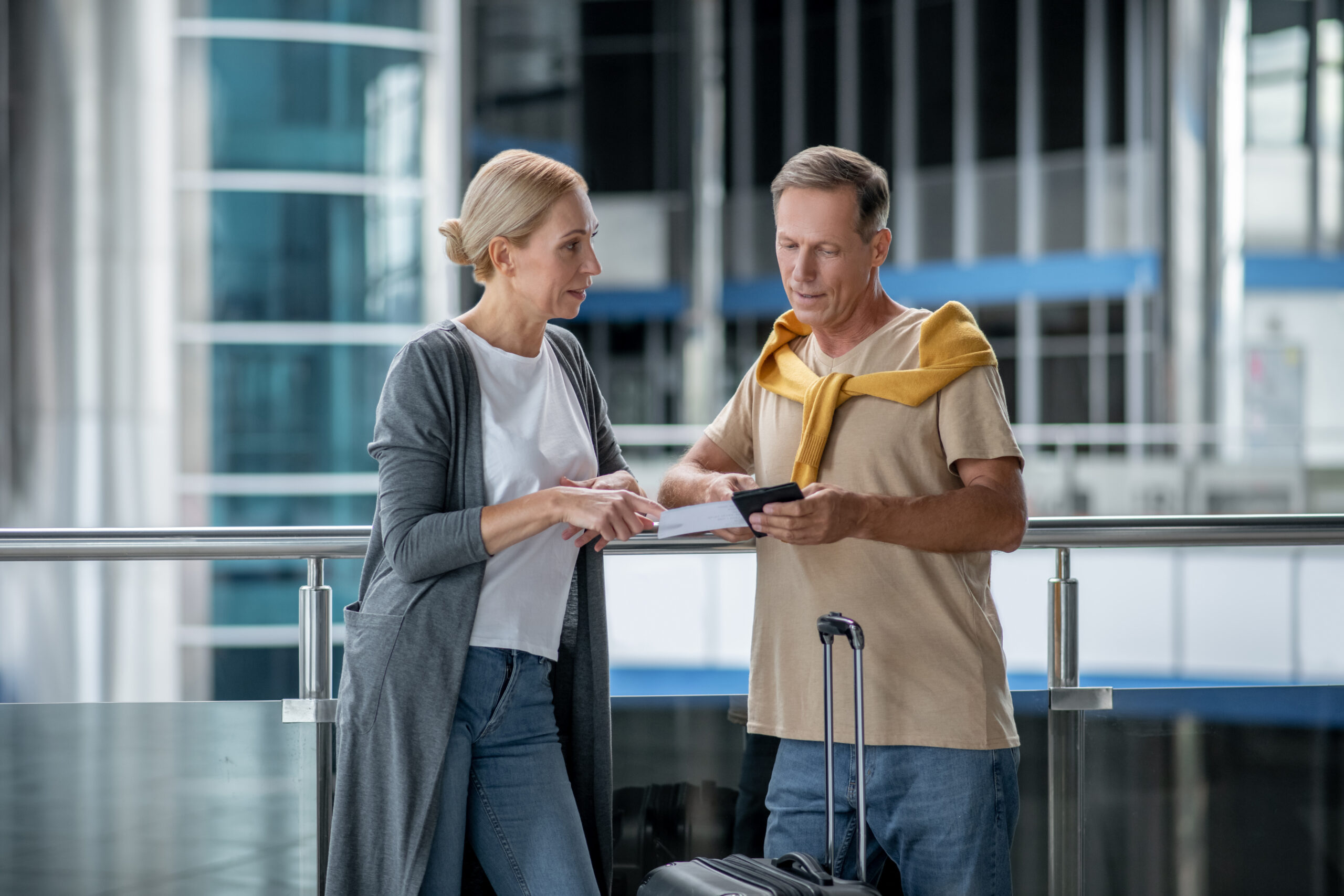 Serious middle-aged woman looking at a man with the boarding ticket and a foreign passport