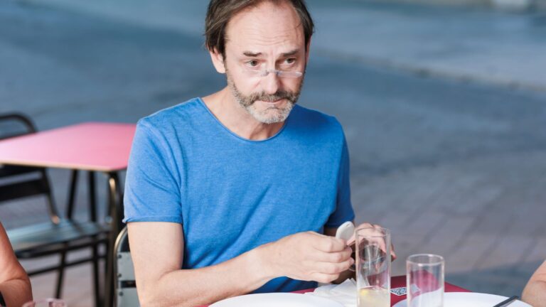 A photo of a Traveler sitting at a restaurant table abroad, slightly unsure, observing others eating.