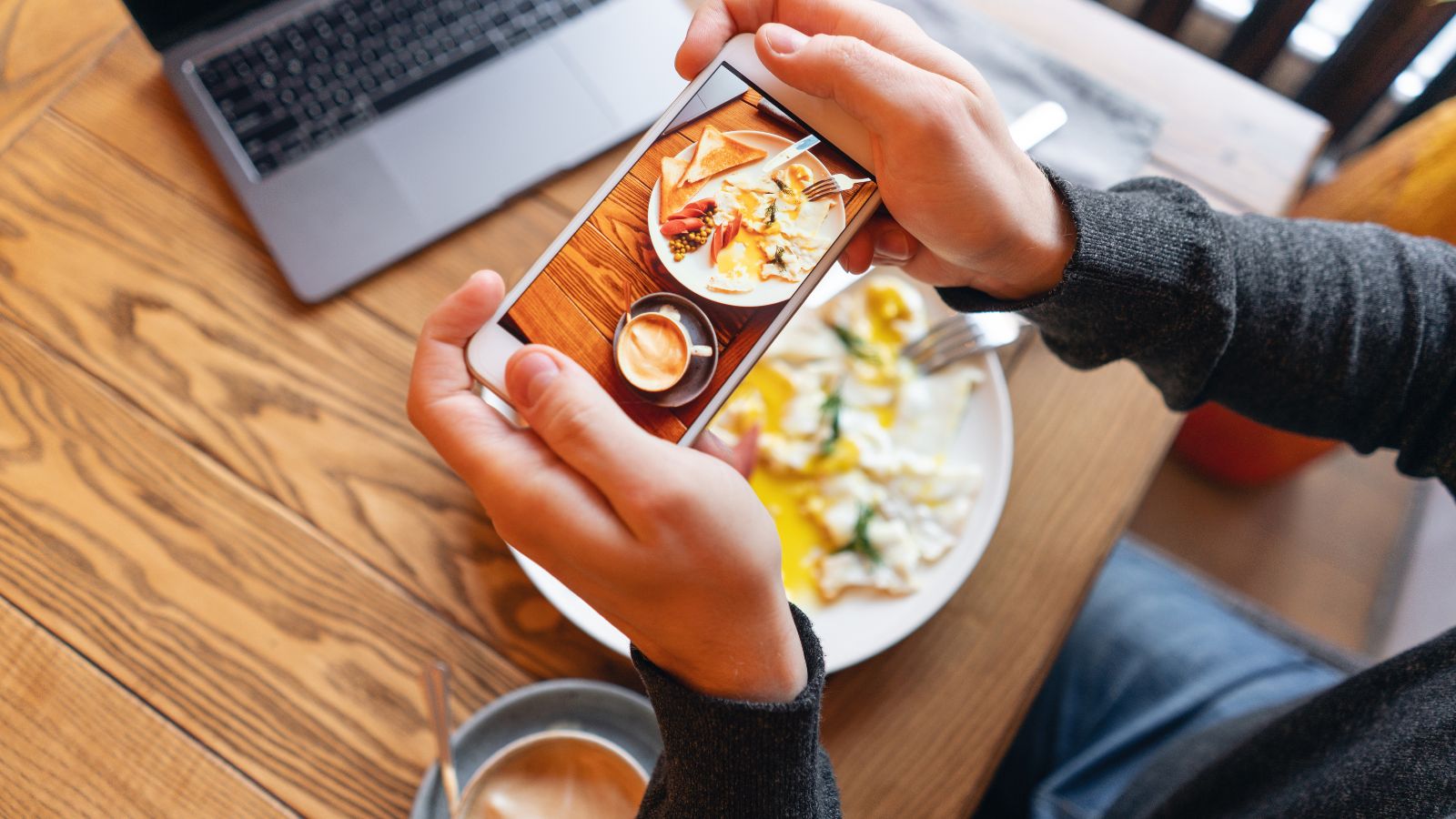 A photo of a man holding a phone taking picture of his food.