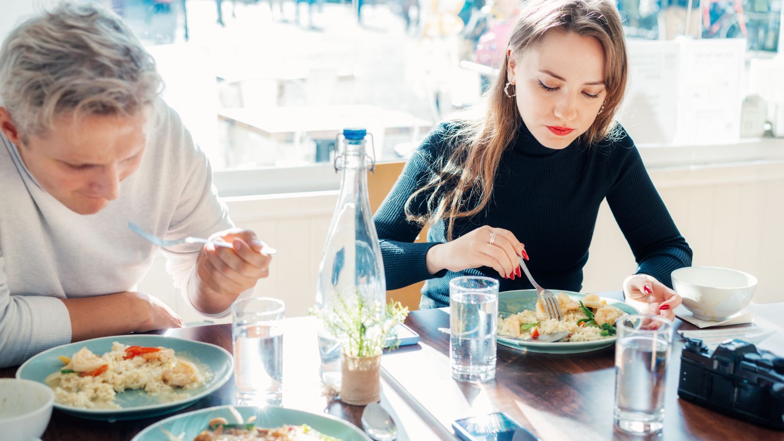 A photo of a woman  eating carefully, observing her plate with a man beside her.