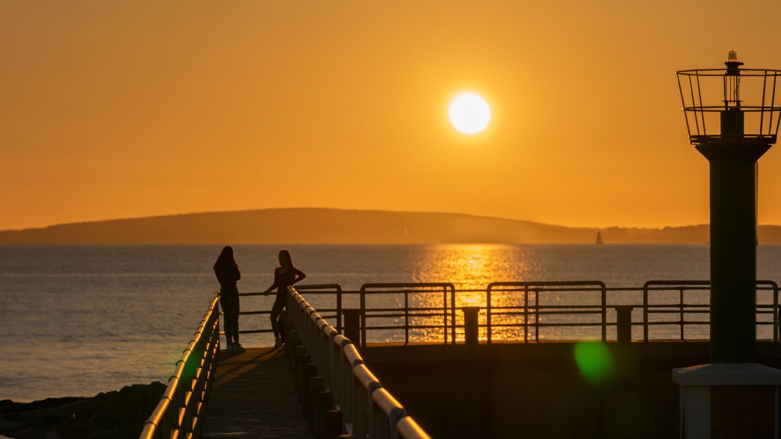 A photo of a couple standing facing each other at the shoreline during golden hour.