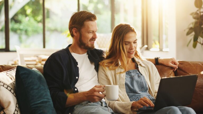 A photo of a couple sitting together with laptop and coffee.